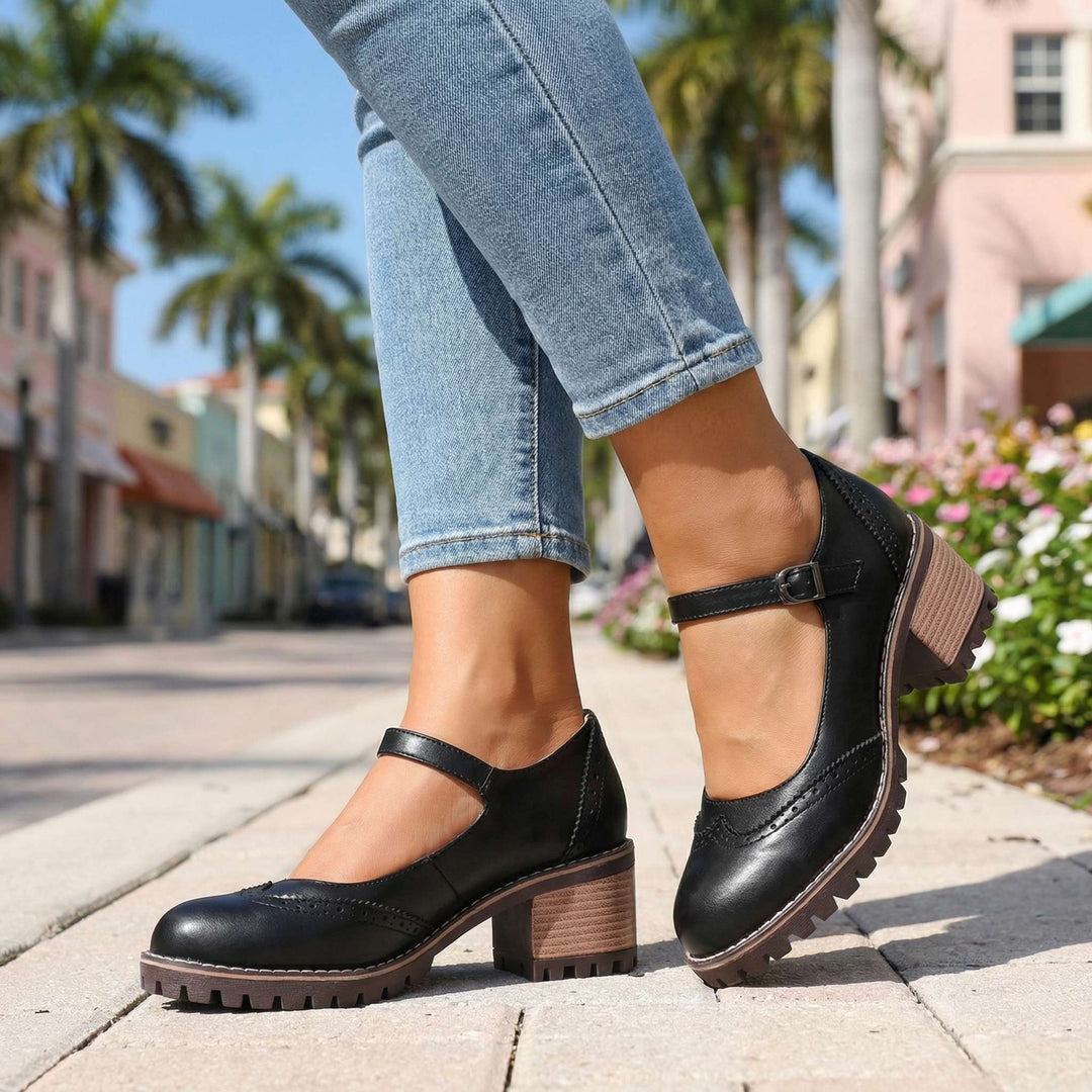 Mary Janes noires portées sur un trottoir fleuri, vue latérale sur la boucle de la bride, le talon bloc et la semelle crantée. 7
