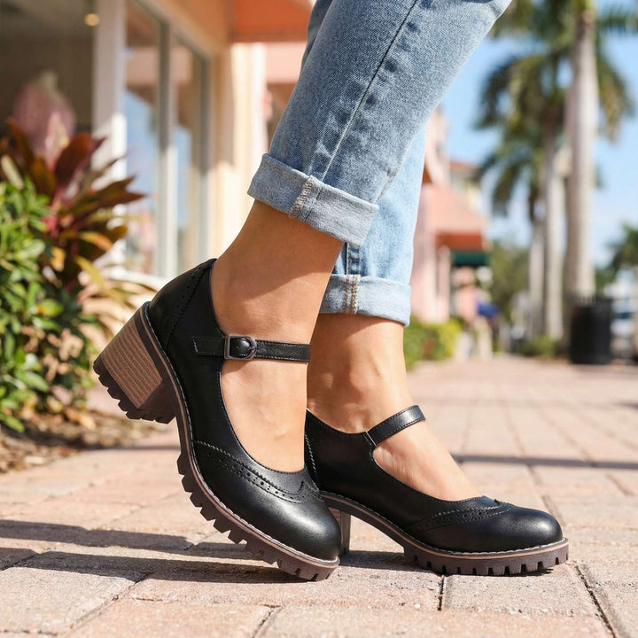 Mary Janes noires portées dehors sur un trottoir pavé, jean retroussé, palmiers et façades colorées floues en arrière-plan. 4
