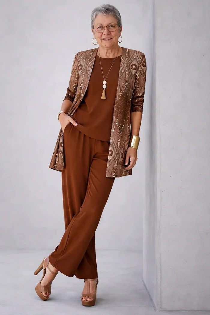 Femme aux cheveux gris, ensemble marron, cardigan à motifs dorés pailletés, appuyée contre un mur en béton 9