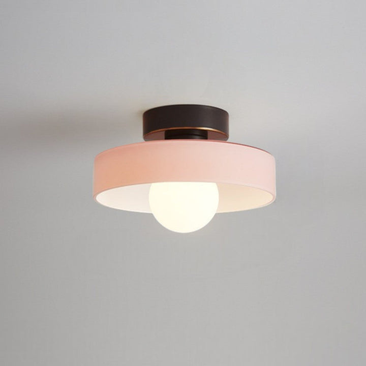 Plafonnier à abat-jour rose pâle et base noire à liseré doré, avec ampoule globe allumée, fixé au plafond. 8