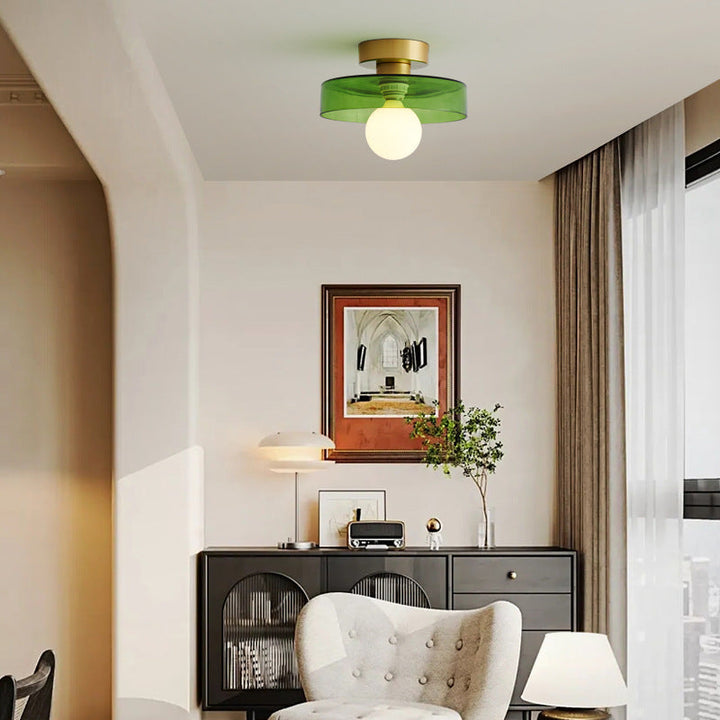Plafonnier à abat-jour en verre vert et base dorée, allumé dans un salon avec fauteuil blanc et buffet noir. 2
