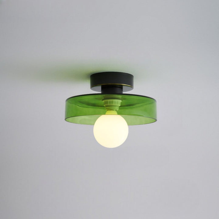 Plafonnier à abat-jour en verre vert transparent, base noire et ampoule globe opaline allumée, vu de près sur fond de plafond gris. 5