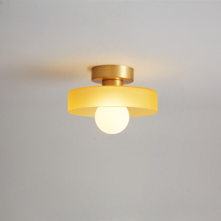 Plafonnier à abat-jour jaune et base dorée en laiton, avec ampoule globe allumée, fixé au plafond. 12
