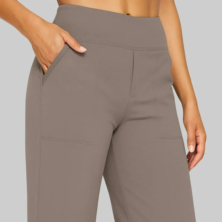 Gros plan sur la taille haute élastique et les poches latérales et plaquées du pantalon taupe, une main dans la poche. 3