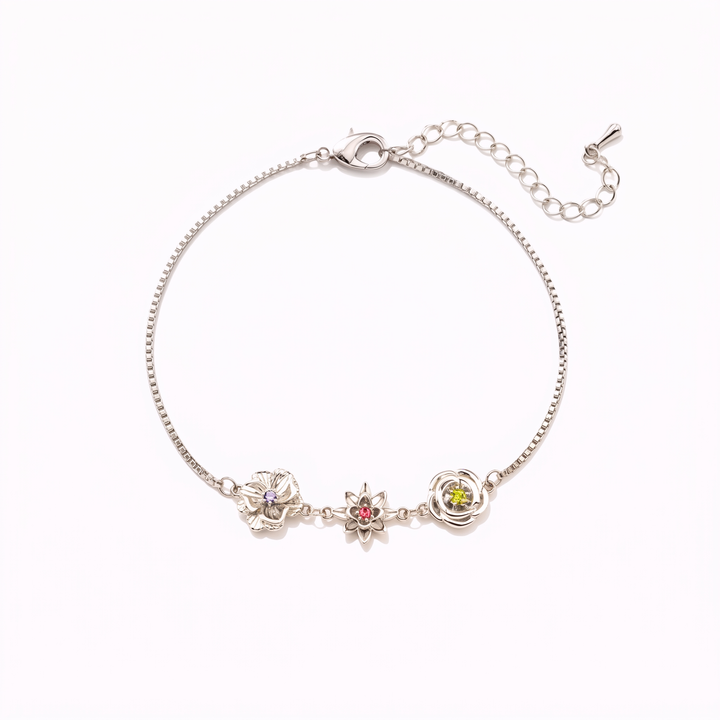 Bracelet argenté vu à plat sur fond blanc, avec trois fleurs serties de pierres violette, rouge et verte et sa chaînette de rallonge. 16