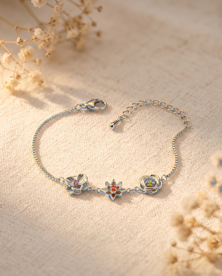 Bracelet argenté posé sur un tissu de lin beige entouré de fleurs séchées, montrant ses trois fleurs et leurs pierres colorées. 13