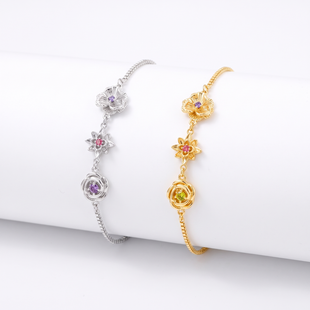 Deux bracelets côte à côte sur un support blanc, l'un argenté et l'autre doré, chacun avec trois fleurs et leurs pierres colorées. 3