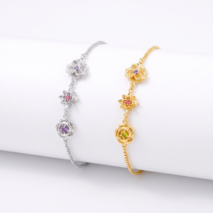 Deux bracelets côte à côte sur un support blanc, l'un argenté et l'autre doré, chacun avec trois fleurs et leurs pierres colorées. 3