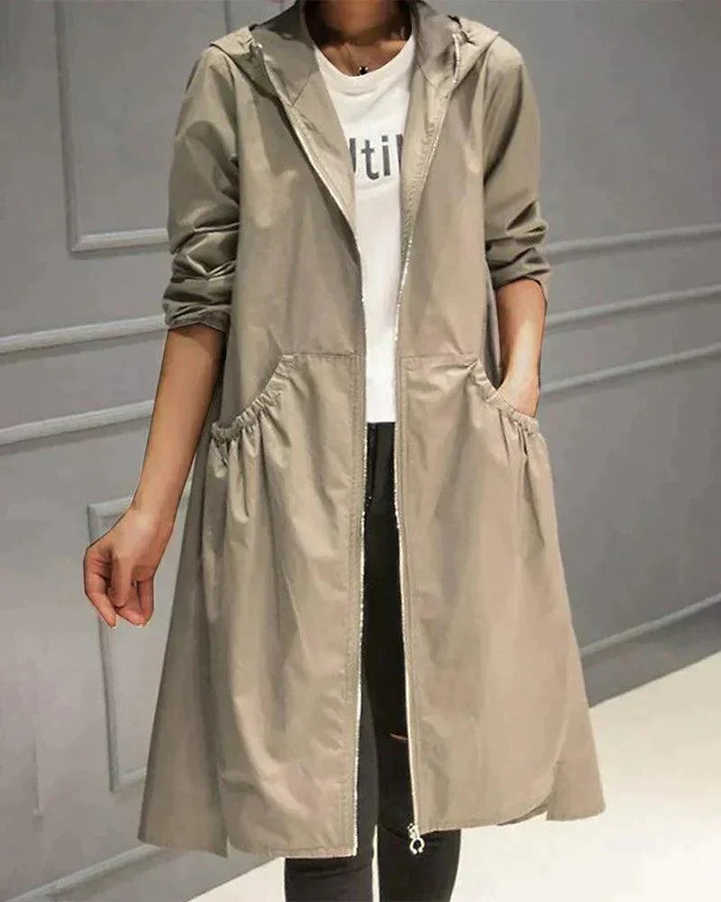 Même imperméable beige vu de face, zip ouvert, mains près des poches froncées, sur fond de boiseries grises 2