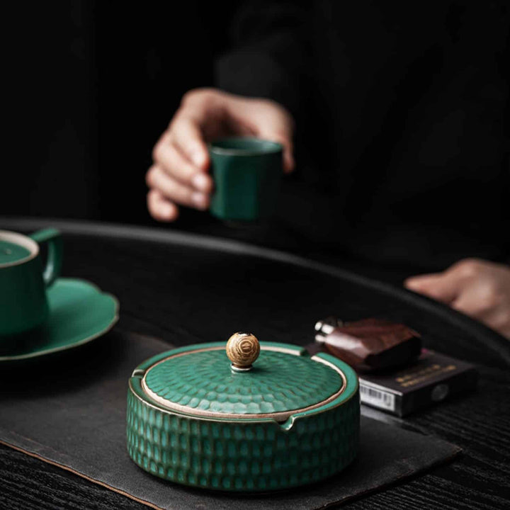 Cendrier vert fermé sur un set de table gris, avec une tasse et une soucoupe vertes et une personne tenant une petite tasse. 4