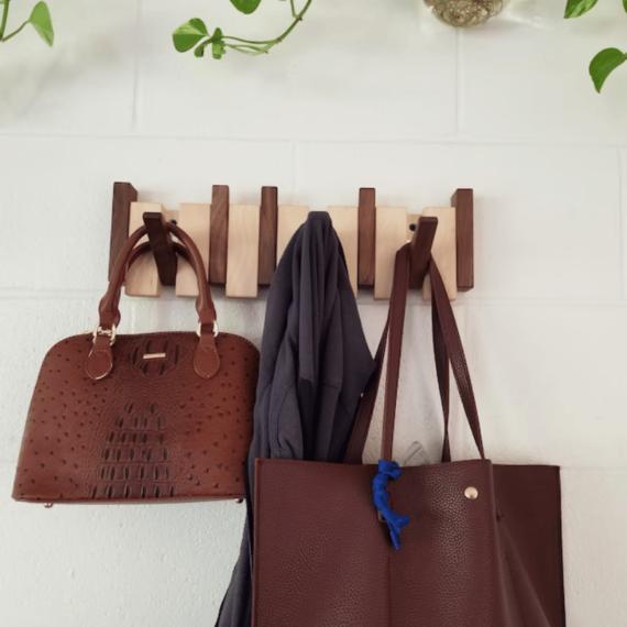 Porte-manteau en bois sur mur de briques blanches, chargé de deux sacs à main bruns et d'une veste 3