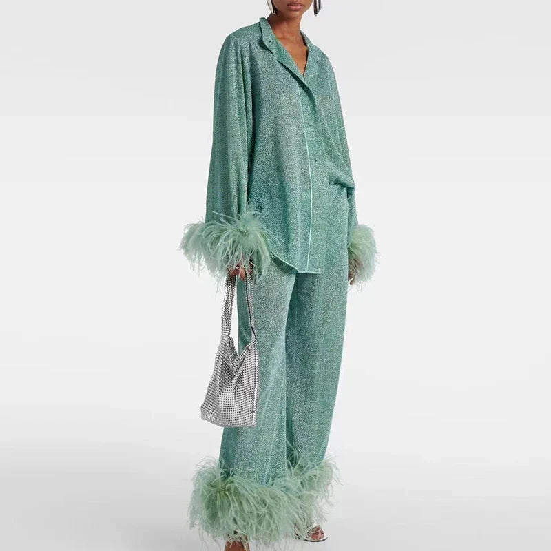 Femme en ensemble vert d'eau pailleté, chemise à col cranté et pantalon large à plumes, tenant un sac à mailles argentées. 2