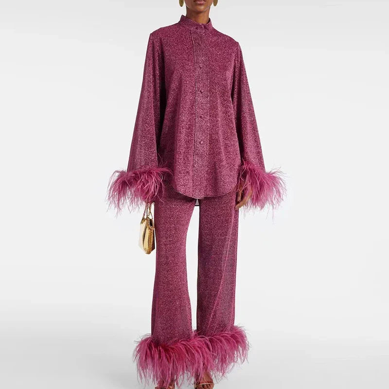 Femme portant l'ensemble bordeaux scintillant, chemise à col montant et pantalon évasé bordés de plumes roses, un petit sac doré à la main. 1