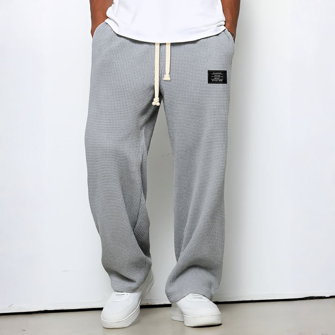 Pantalon ample gris clair en maille gaufrée, mains dans les poches, porté avec baskets blanches 6