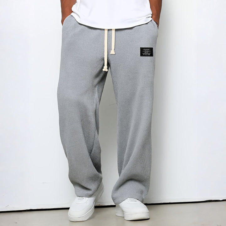 Pantalon ample gris clair en maille gaufrée, mains dans les poches, porté avec baskets blanches 6