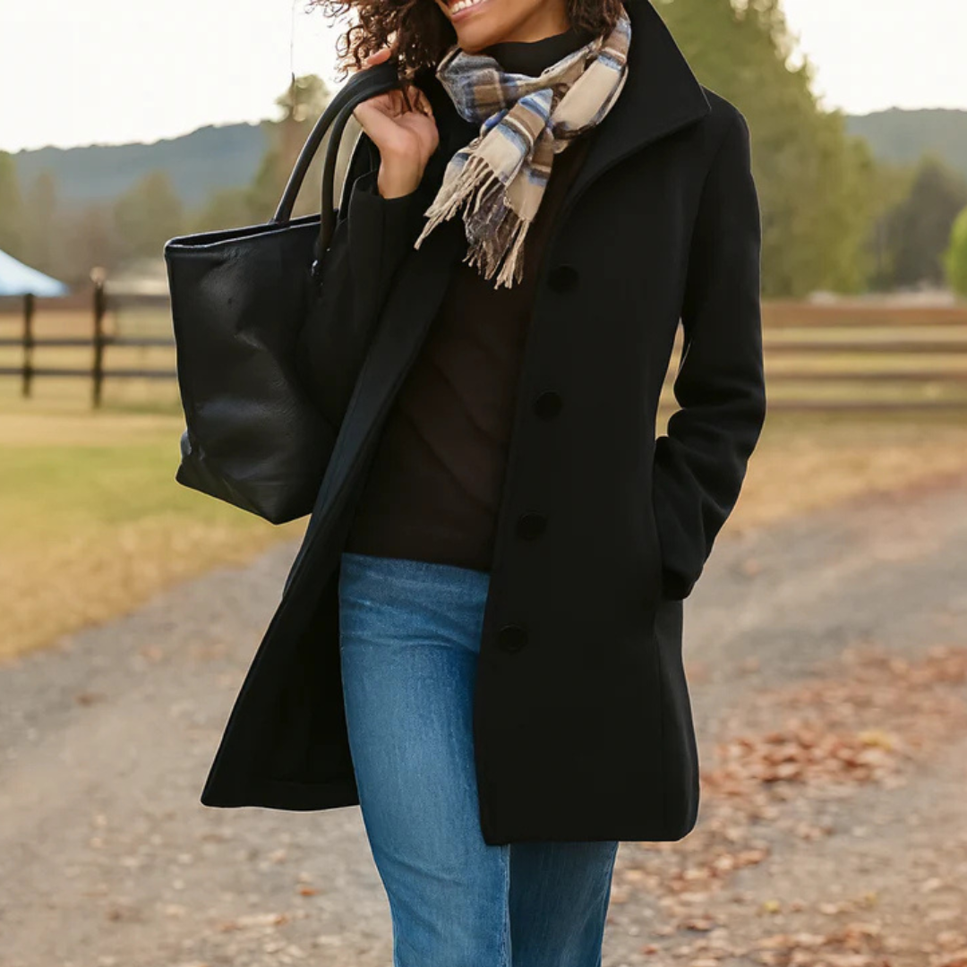 Version noire du manteau boutonné portée avec jean, écharpe à carreaux et sac noir, sur un chemin de campagne bordé de clôtures. 3