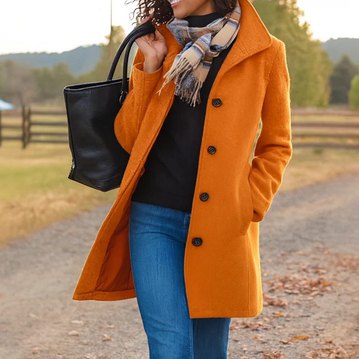 Manteau orange citrouille à col relevé, porté avec pull noir, jean et écharpe à franges, sur un chemin couvert de feuilles. 7