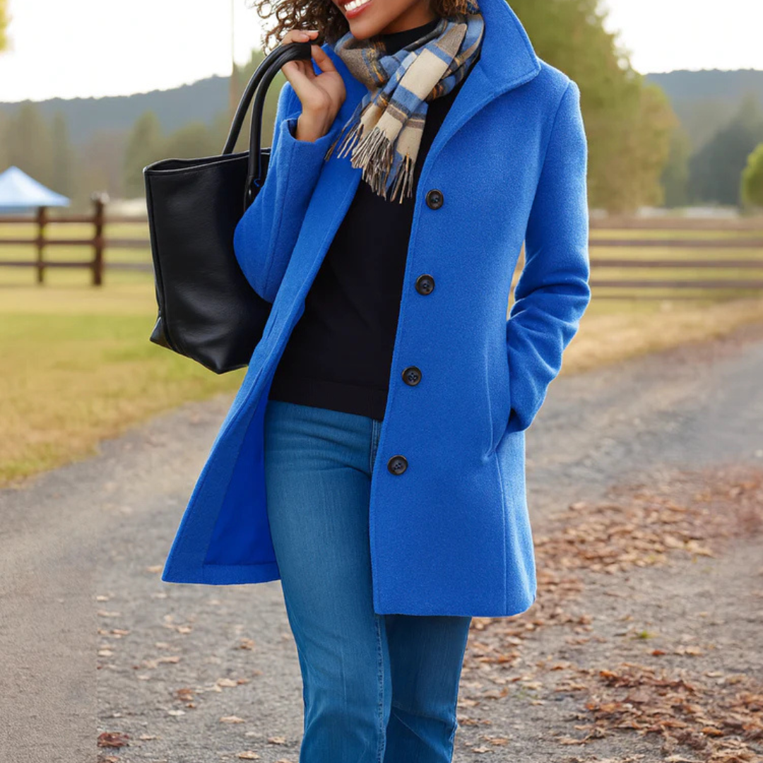 Manteau bleu roi boutonné porté avec un jean, une écharpe à carreaux et un sac noir, devant une clôture en bois. 8