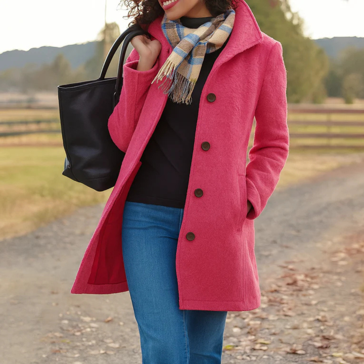 Manteau rose framboise à boutons marron porté par une femme souriante, avec pull noir, jean, écharpe à carreaux et sac noir. 9