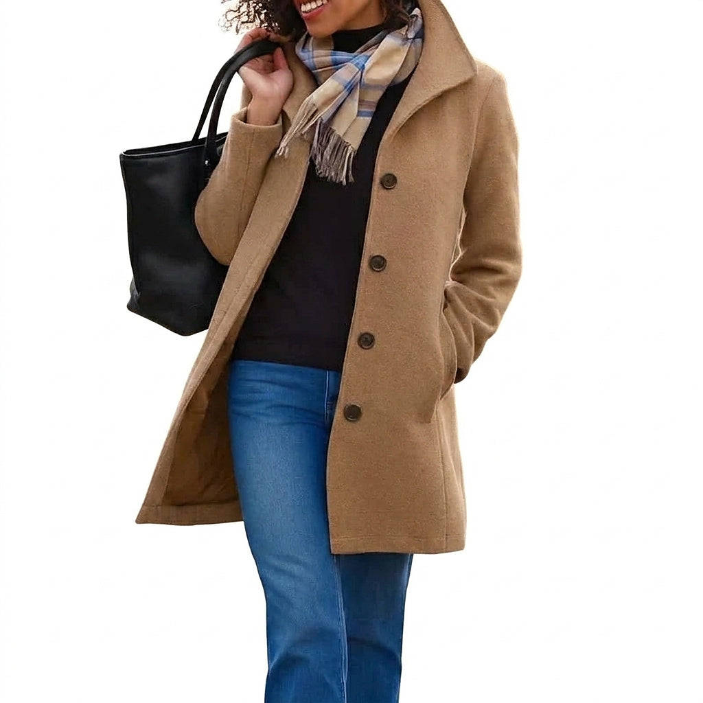 Femme portant le manteau camel boutonné avec col montant, pull noir, jean et écharpe à carreaux, sac noir à l'épaule, fond uni blanc. 1