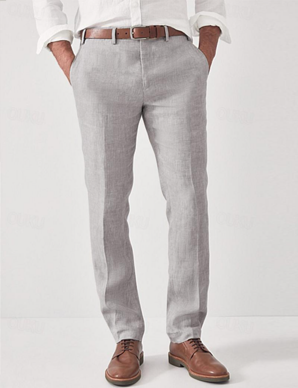 Pantalon en lin gris clair porté par un modèle avec chemise blanche, ceinture marron et chaussures en cuir, mains dans les poches. 2
