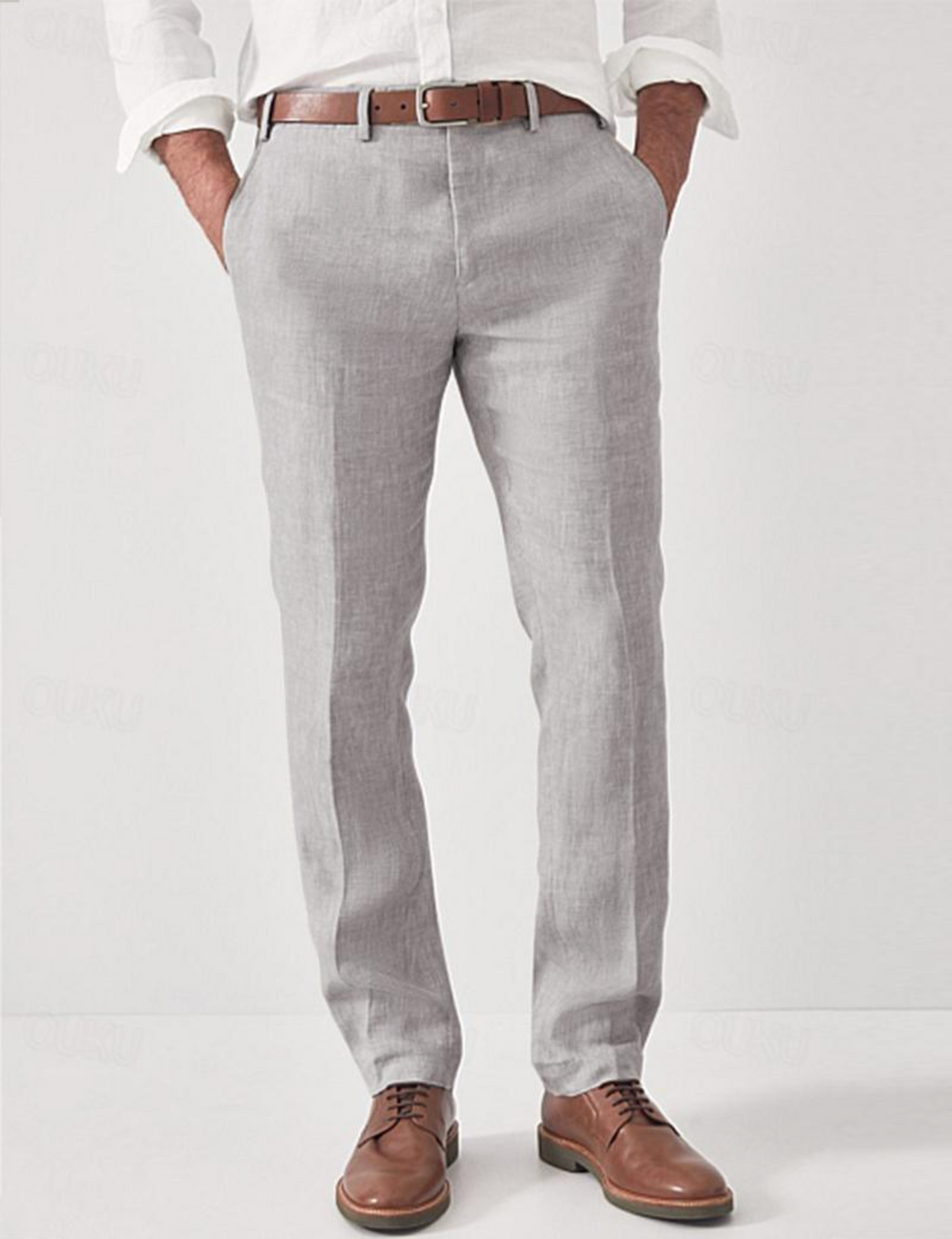 Pantalon en lin gris clair porté par un modèle avec chemise blanche, ceinture marron et chaussures en cuir, mains dans les poches. 2