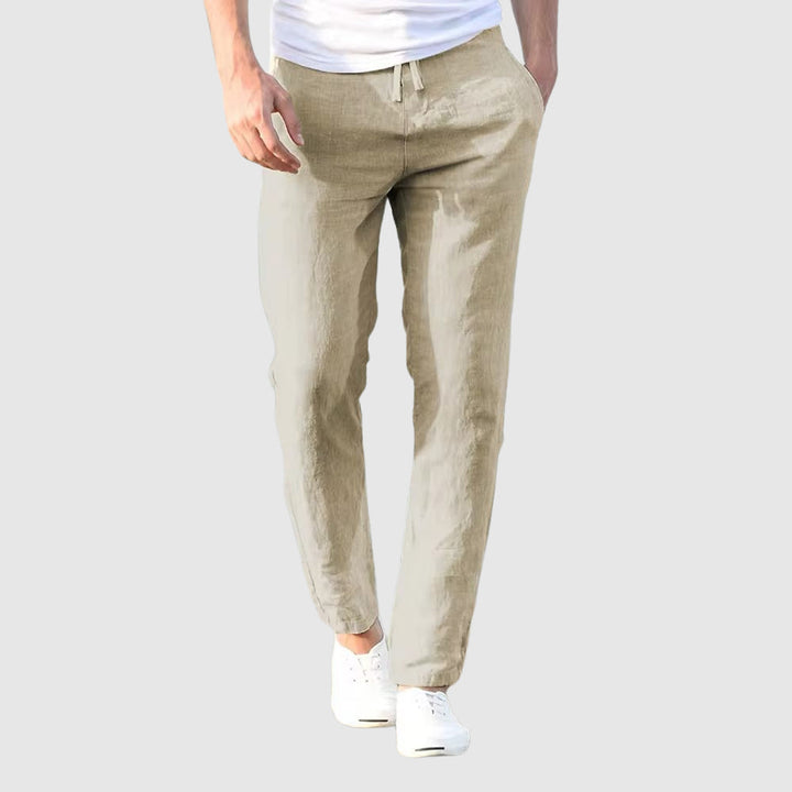 Vue de face du pantalon beige clair en lin porté par un modèle, avec cordon à la taille et baskets blanches. 2