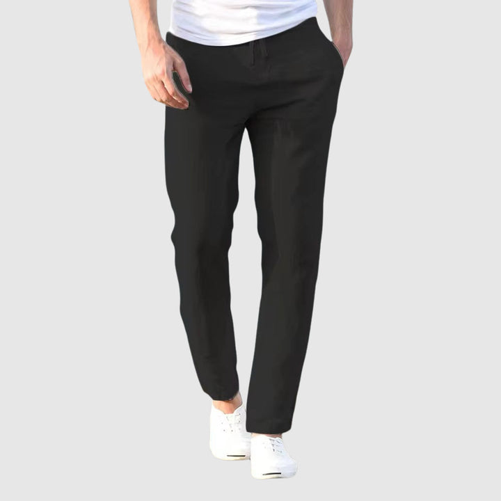 Vue de face du pantalon noir porté par un modèle en t-shirt blanc et baskets blanches, cordon à la taille. 4