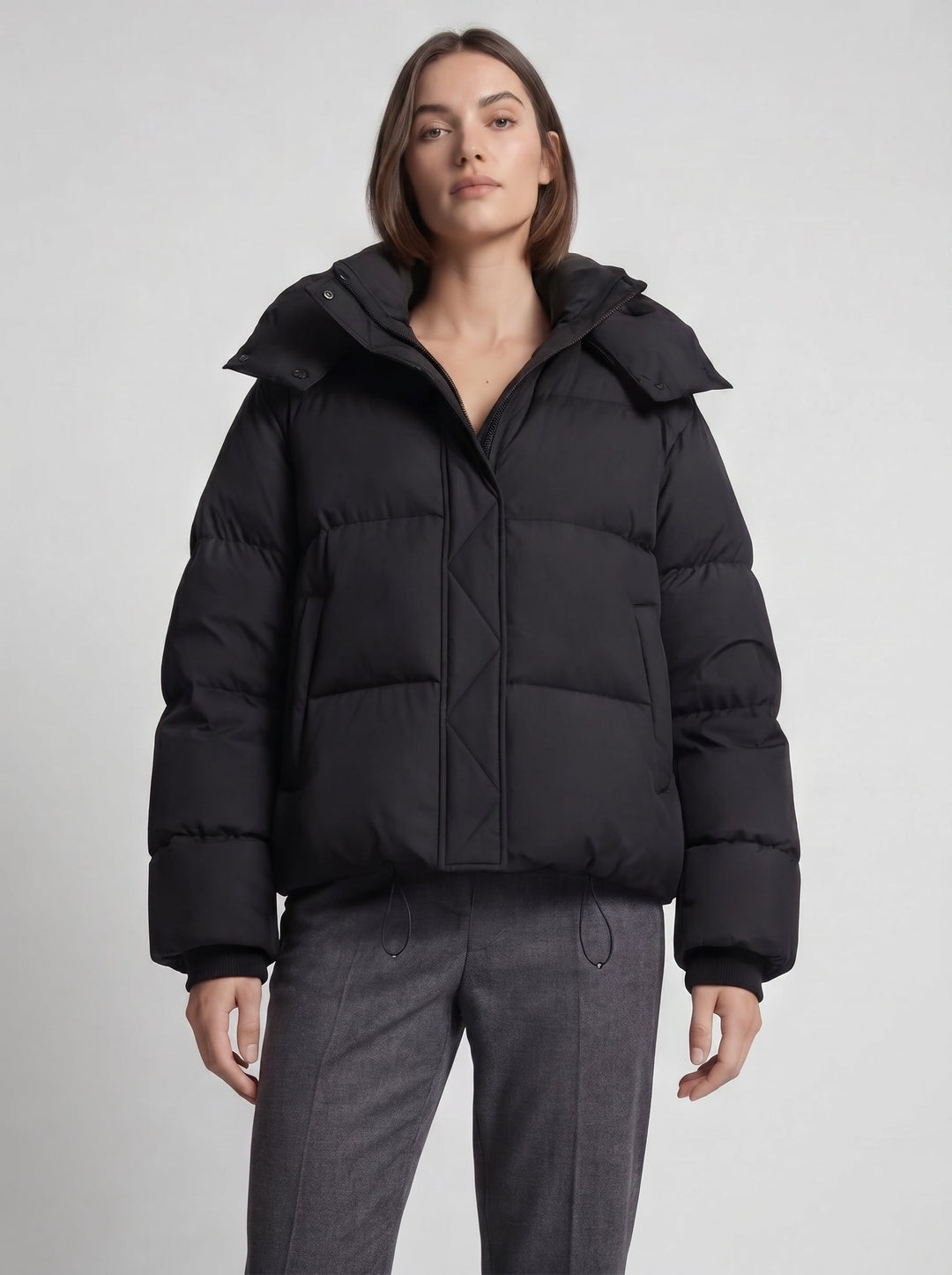 Mannequin de face en doudoune noire fermée, pantalon gris, cordons de serrage visibles à la taille 6