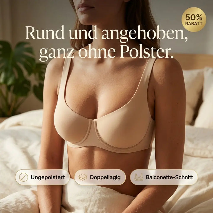 Femme assise sur un lit portant le soutien-gorge balconnet beige sans rembourrage, plan de face dans une chambre lumineuse avec plante verte. 1
