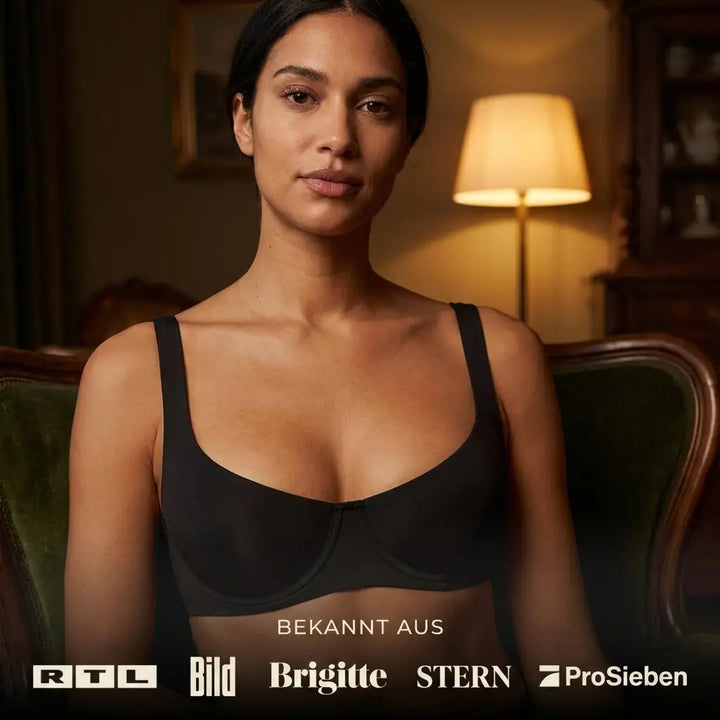 Femme assise dans un fauteuil vert portant le soutien-gorge balconnet noir, vue de face, avec logos de médias en bas. 4
