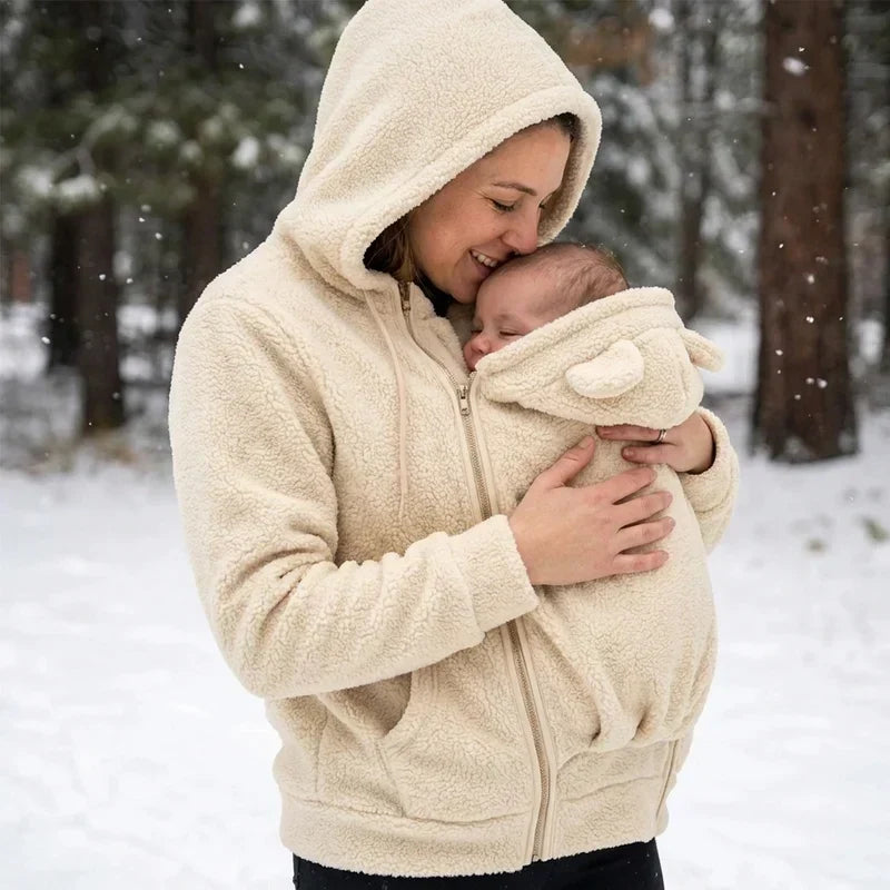 Femme en sweat beige capuche relevée embrassant le front de son bébé niché dans l'empiècement, sous la neige. 16