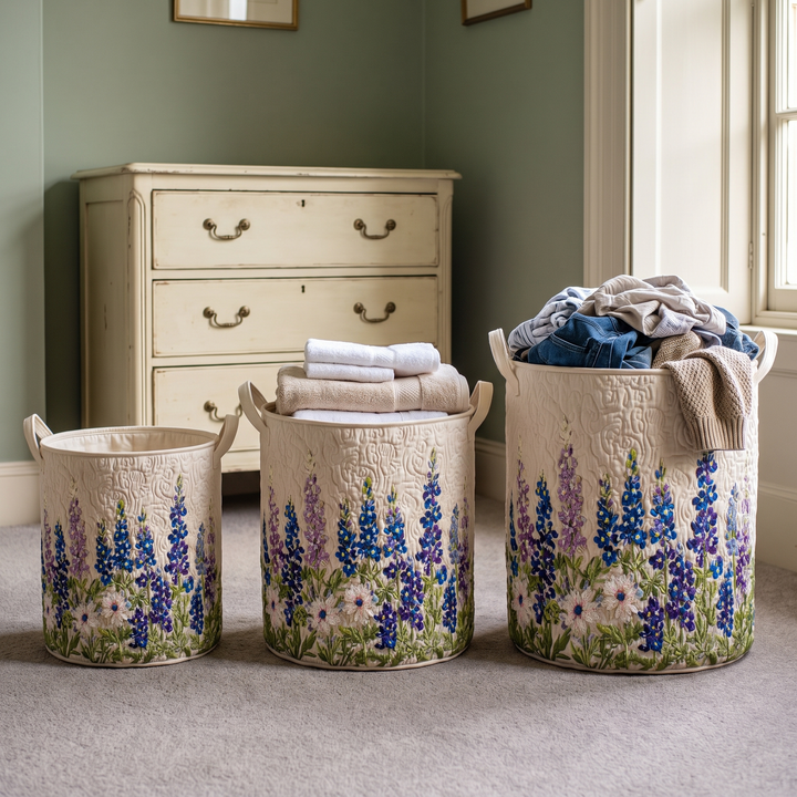 Trois paniers brodés de fleurs de tailles différentes alignés sur une moquette devant une commode ancienne, remplis de serviettes et de vêtements. 3