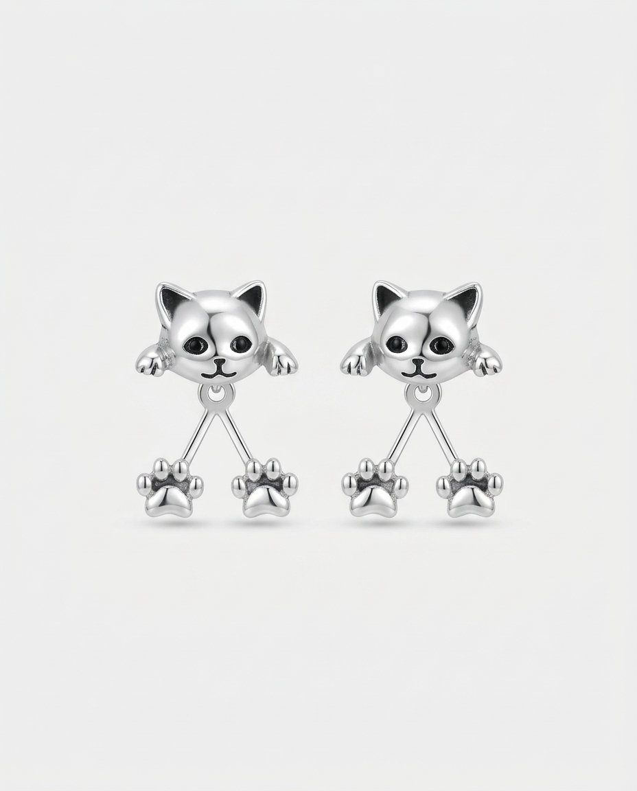 Paire de boucles d'oreilles argentées, têtes de chat aux yeux noirs et deux pattes pendantes, sur fond blanc 1