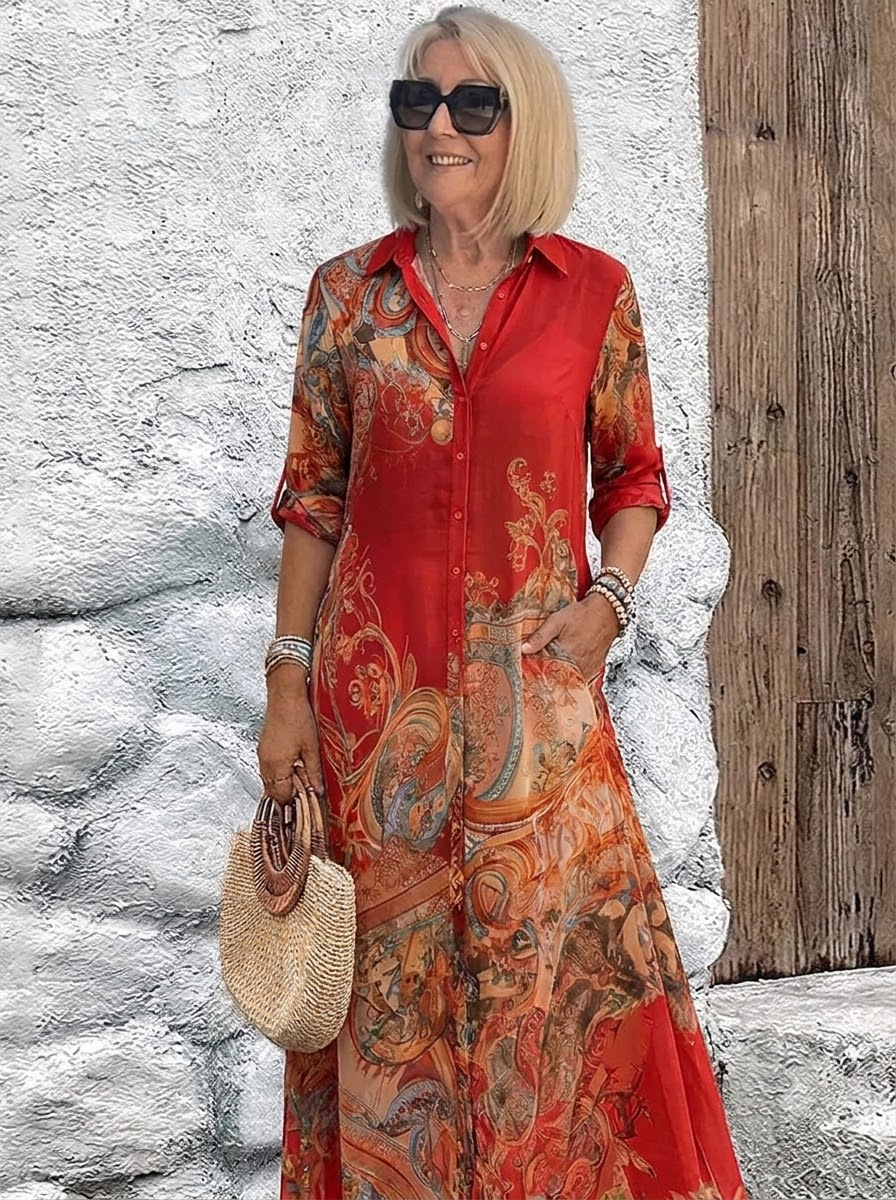 Robe chemise longue portée en rouge vif à motifs baroques orangés, col chemise et boutonnage devant, sac en paille à la main. 3