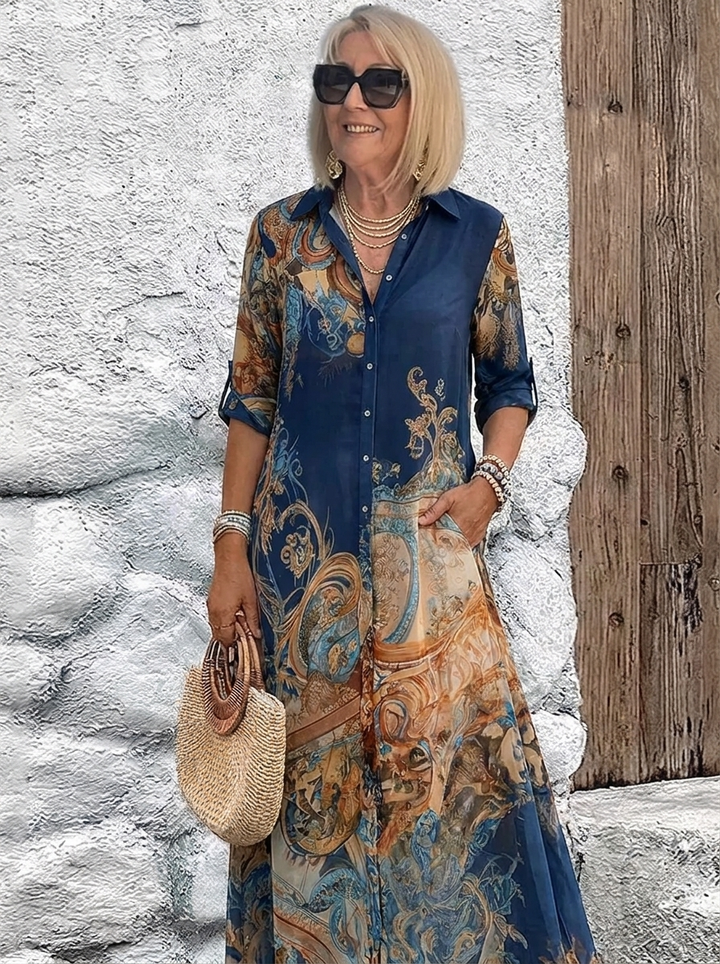 Même robe chemise longue portée en bleu marine, avec motifs baroques dorés et cuivrés, manches retroussées et sac rond en paille. 2