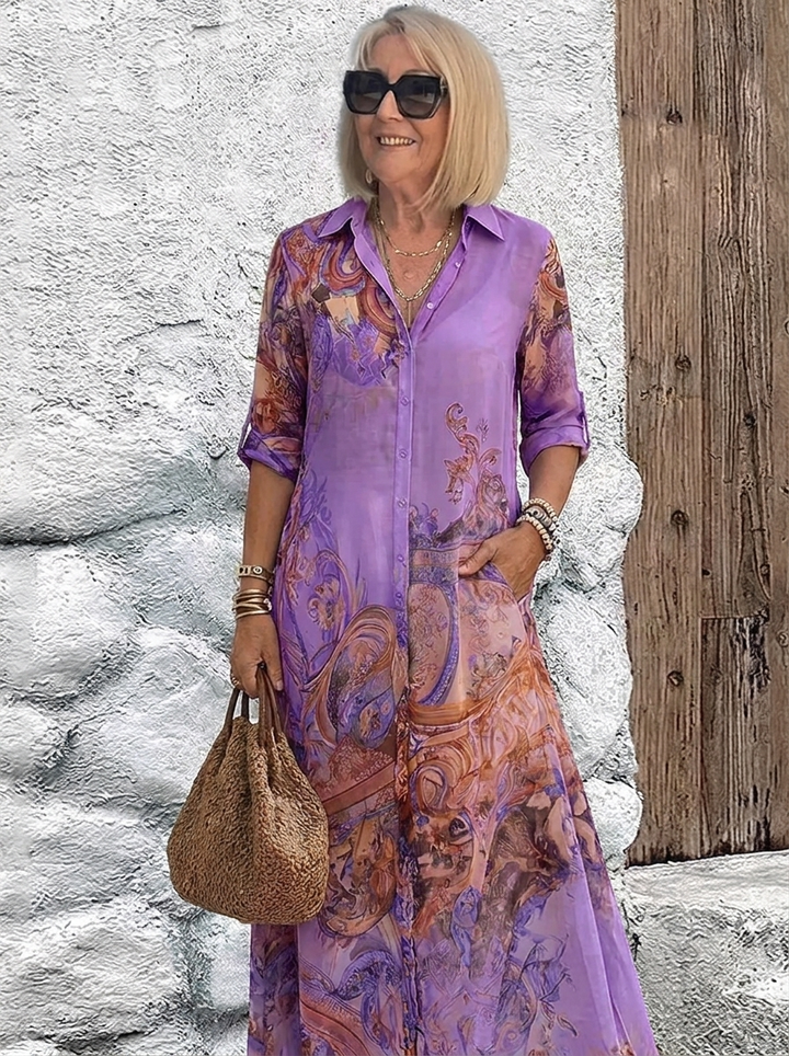 Robe chemise longue portée en violet à motifs baroques cuivrés, mannequin avec un sac en paille souple et des bracelets. 5
