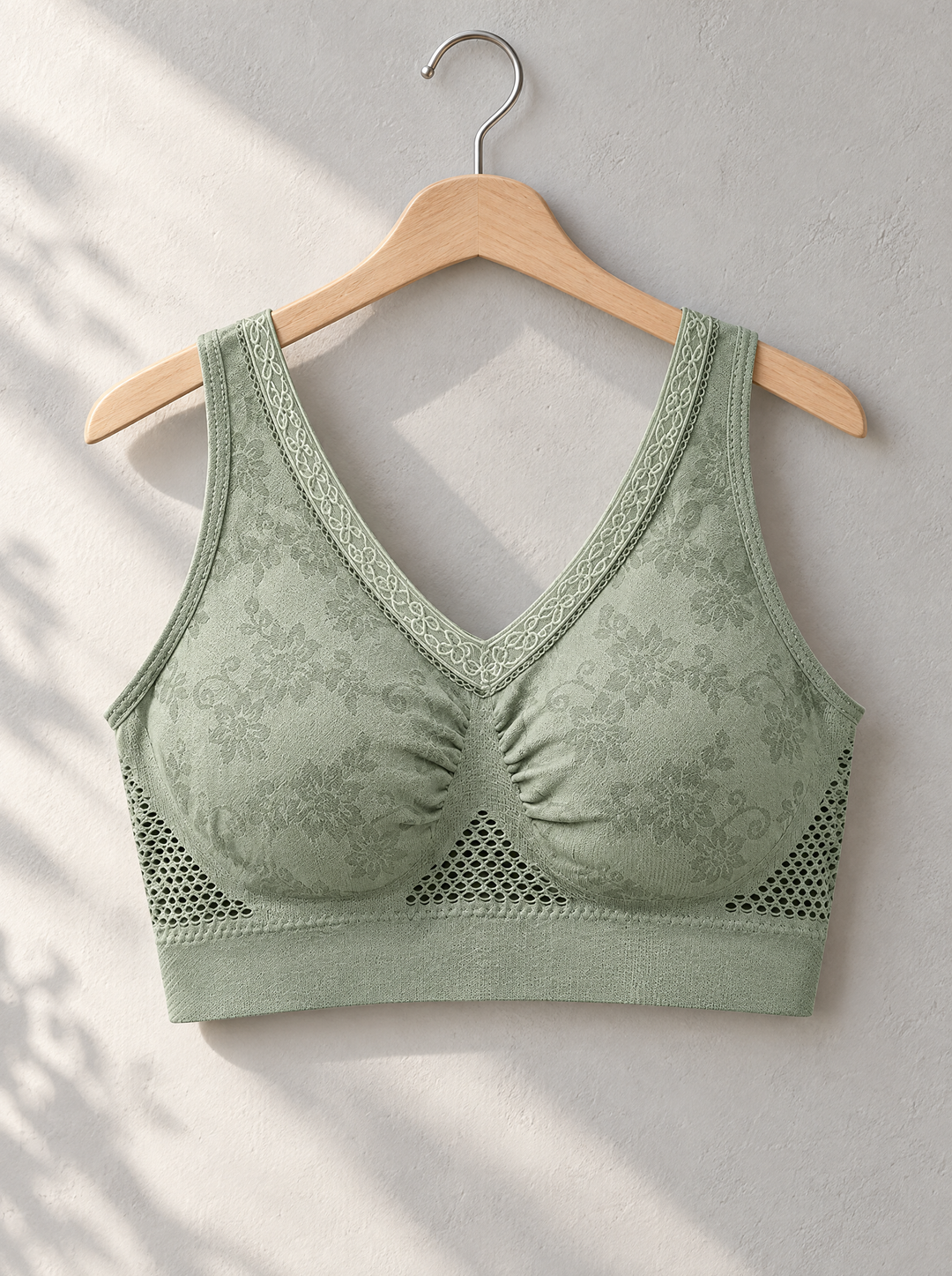 Soutien-gorge vert sauge suspendu à un cintre en bois contre un mur clair, vue de face 4
