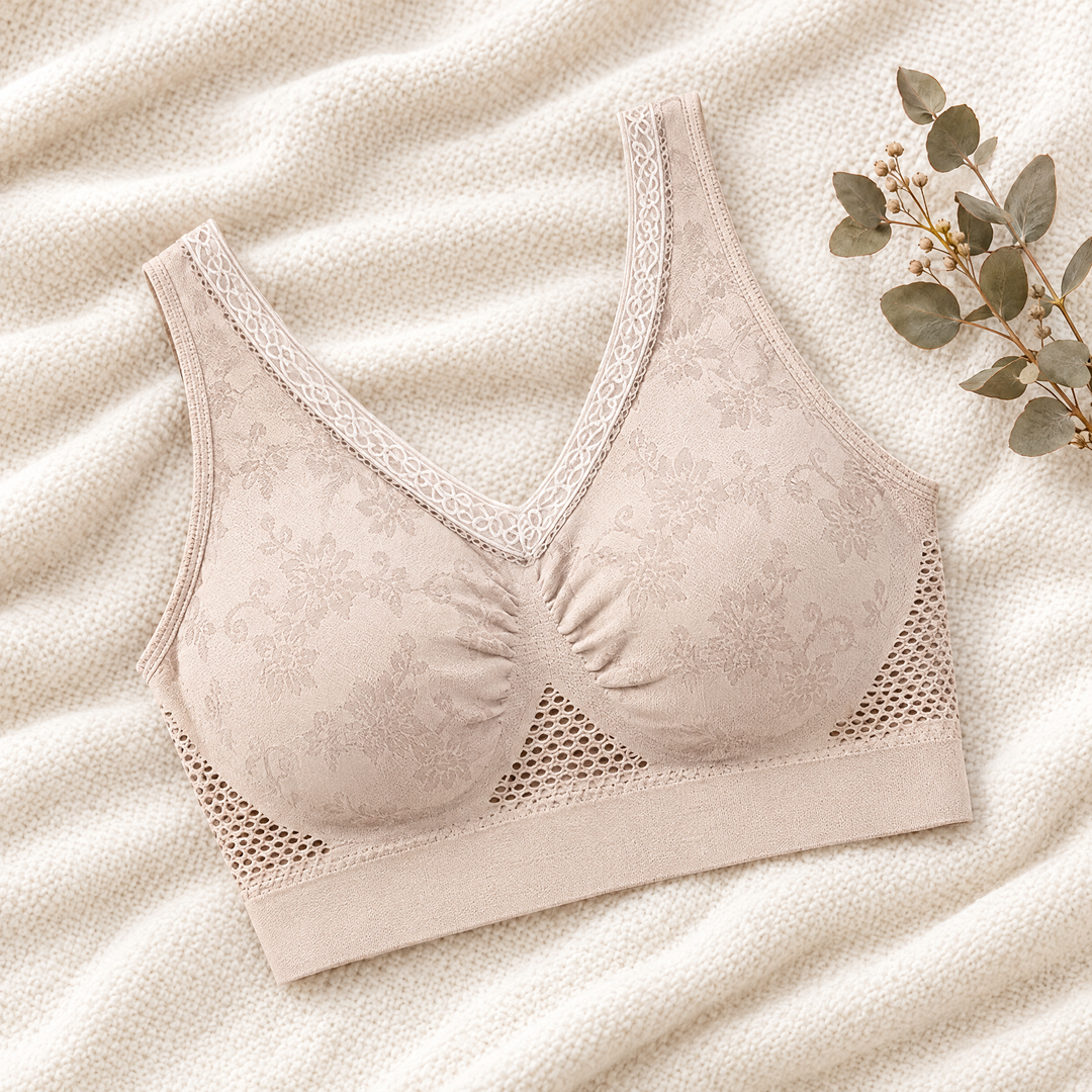 Soutien-gorge beige à dentelle florale et zones ajourées, posé à plat sur un plaid avec une branche d'eucalyptus 1