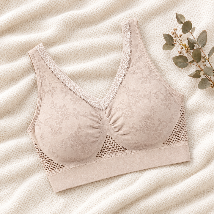 Soutien-gorge beige à dentelle florale et zones ajourées, posé à plat sur un plaid avec une branche d'eucalyptus 1