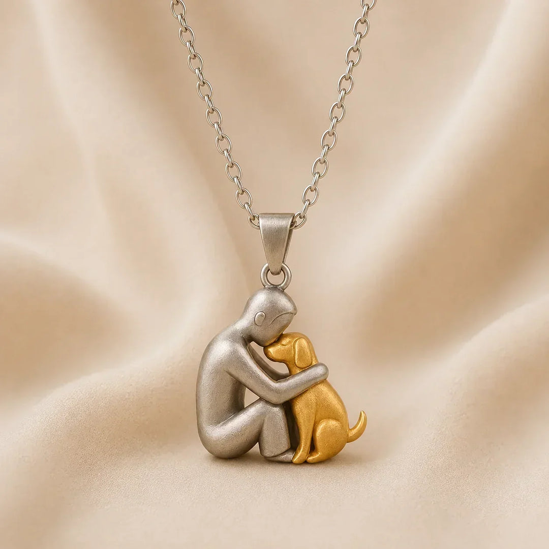 Vue de profil du pendentif mat : une personne argentée front contre front avec un chien doré assis, sur tissu crème. 6