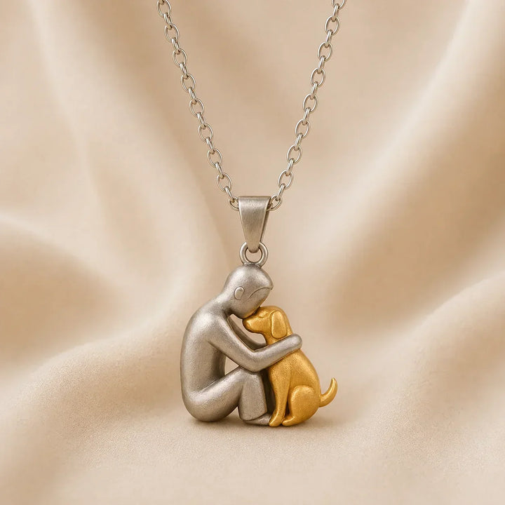 Vue de profil du pendentif mat : une personne argentée front contre front avec un chien doré assis, sur tissu crème. 6