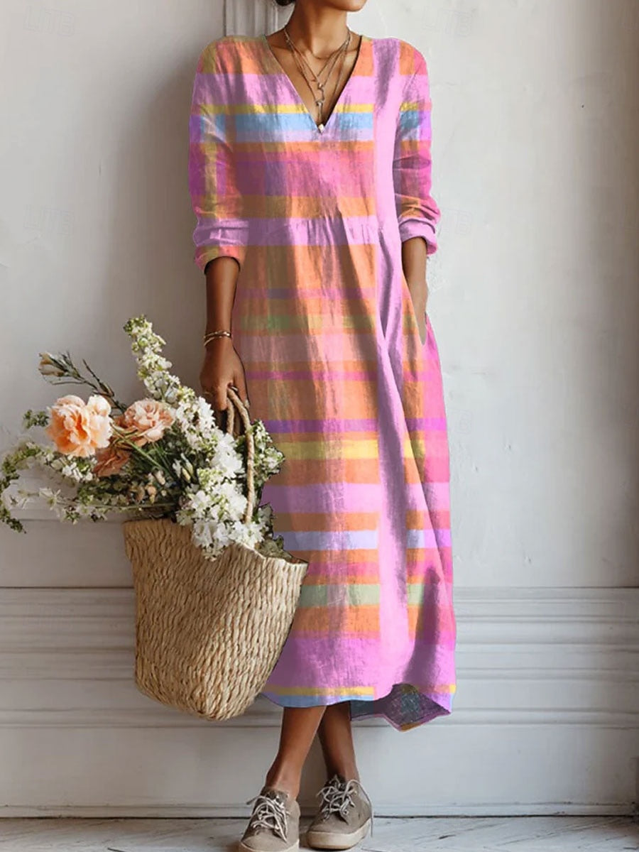Femme portant la robe mi-longue à col en V et manches longues, motif à carreaux rose et orange, une main dans la poche, avec un panier en paille fleuri. 1