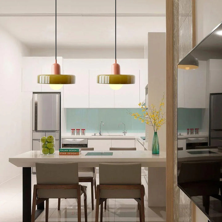 Deux suspensions à verre vert olive et capuchon rose au-dessus d'un îlot de cuisine blanche moderne avec chaises en bois. 27