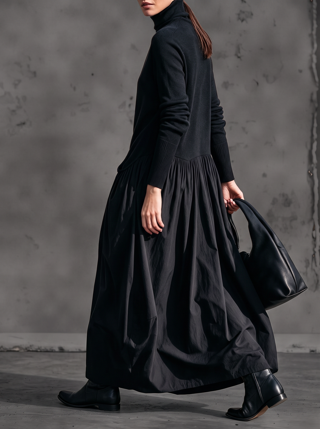 Mannequin en marche vue de trois quarts, robe noire ample à jupe froncée, bottines et sac 2