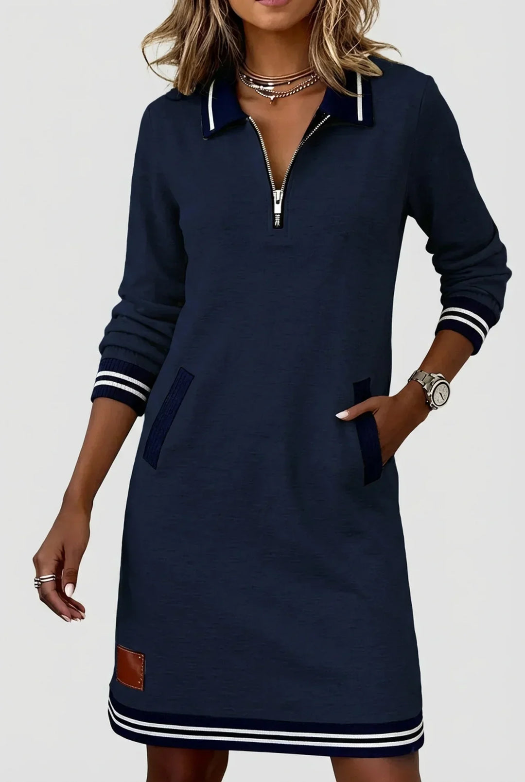 Robe bleu marine portée de face par un mannequin, main dans la poche, zip argenté au col et ourlet rayé. 8