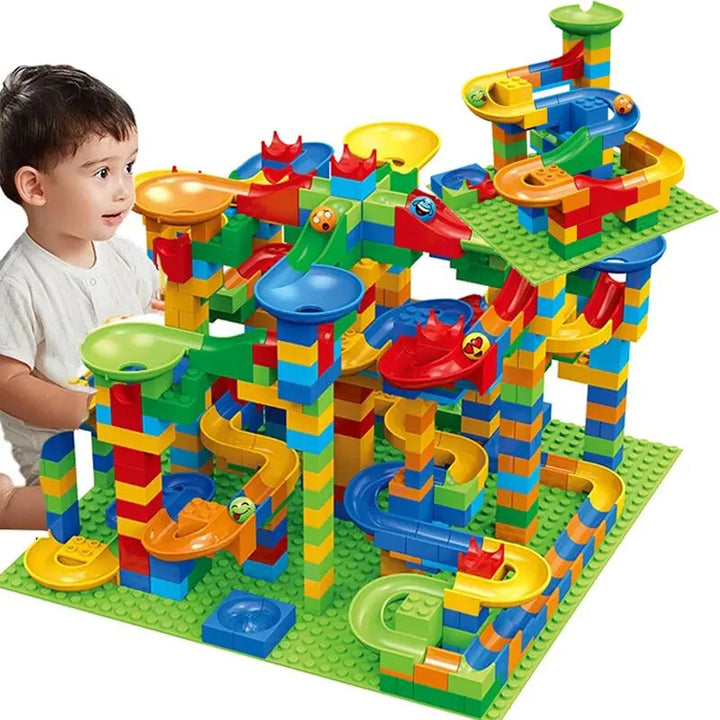 Jeune enfant regardant avec curiosité un grand circuit de billes coloré à étages, monté sur deux plaques vertes. 6