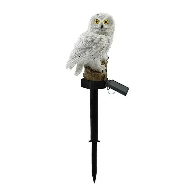 Hibou blanc aux yeux jaune orangé sur sa souche, vu de face avec son piquet noir et son petit panneau solaire articulé. 15
