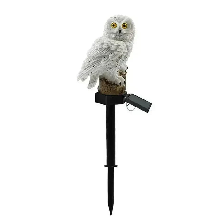 Hibou blanc aux yeux jaune orangé sur sa souche, vu de face avec son piquet noir et son petit panneau solaire articulé. 15