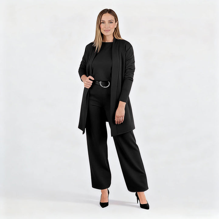 Ensemble noir porté par une mannequin en pied sur fond blanc, cardigan ouvert, ceinture à boucle ronde, escarpins noirs. 15
